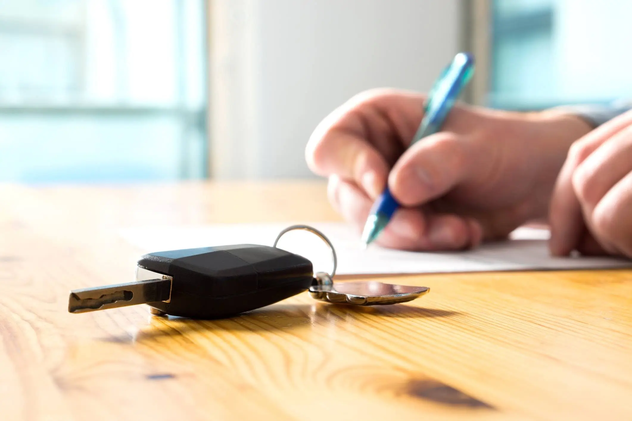 A person signing paperwork with car keys