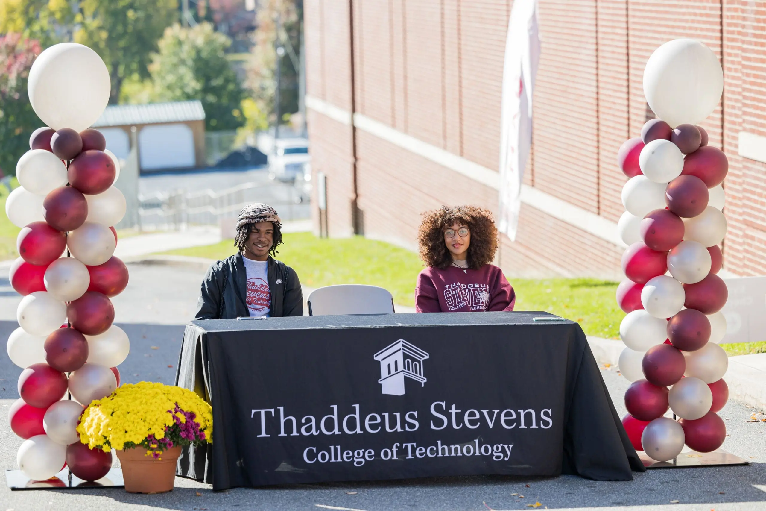 Thaddeus Stevens College students sitting and smiling at Thaddeus Stevens College of Technology table with balloons and flowers around