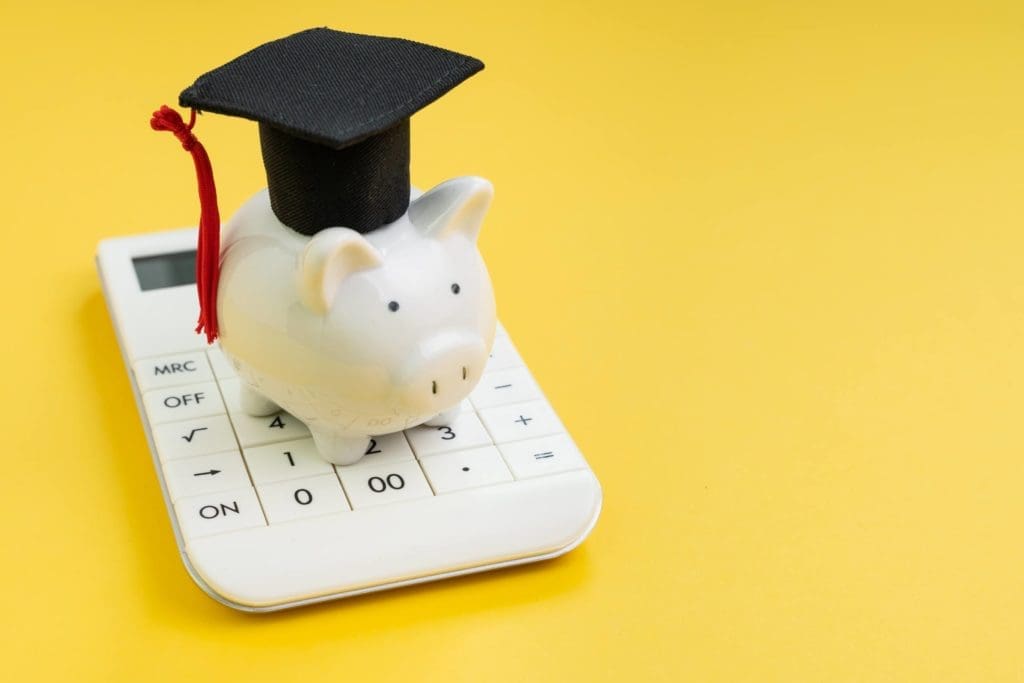 a piggybank with a graduation cap standing on a calculator. 