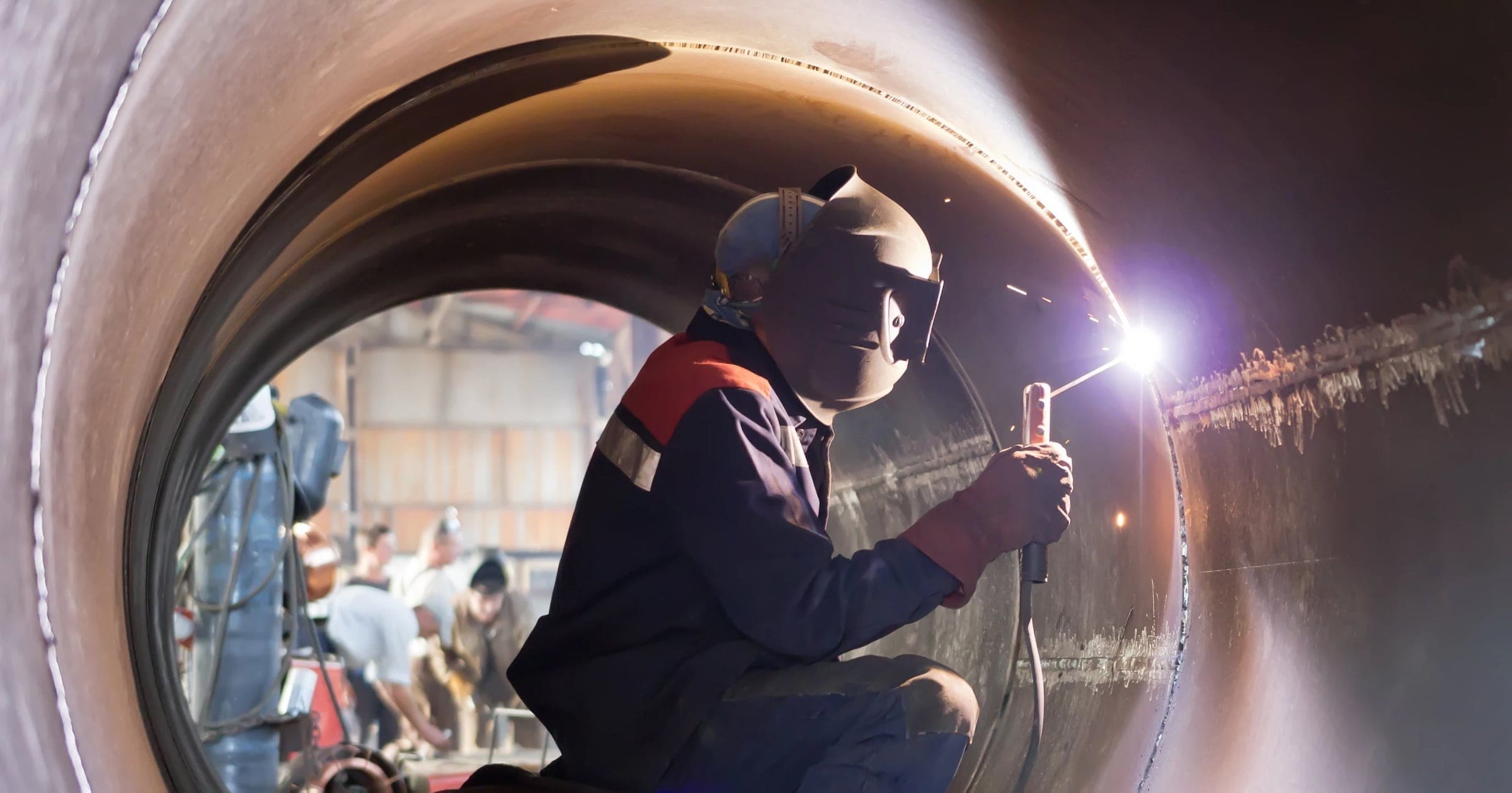 A welder works within a large pipe.